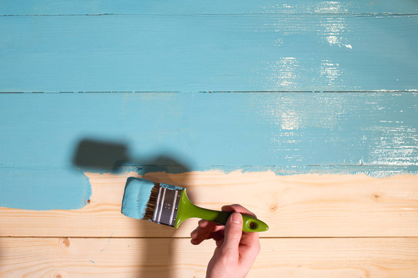 Man hand paints wooden board to blue color - Φωτογραφία, εικόνα