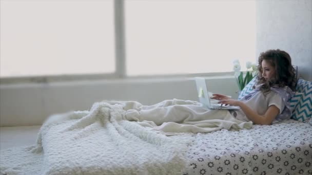 Mujer joven descansando en la cama viendo las redes sociales en Internet en un ordenador portátil
. - Metraje, vídeo