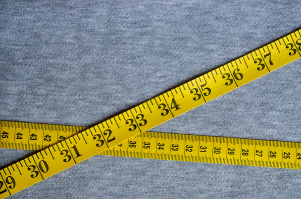 Yellow measuring tape lies on a gray knitted fabric - Photo, Image