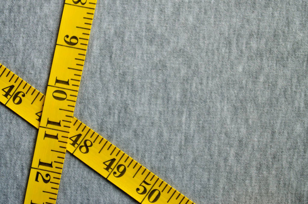A fita métrica amarela está em um tecido de malha cinza
 - Foto, Imagem
