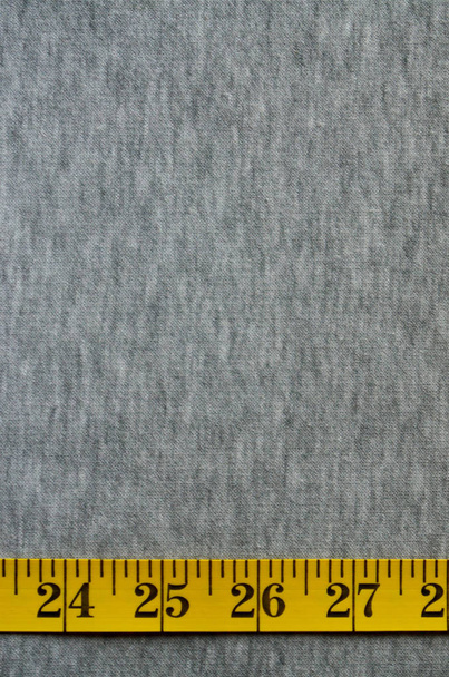 Κίτρινη ταινία μέτρησης βρίσκεται σε ένα γκρι πλεκτό ύφασμα - Φωτογραφία, εικόνα
