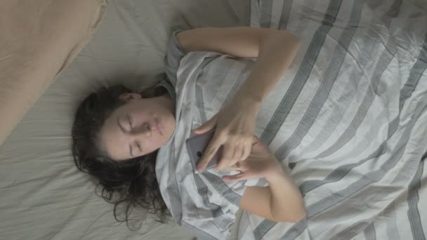 Young woman in bed wakes up in the morning and on the phone . The view from the top - Filmati, video