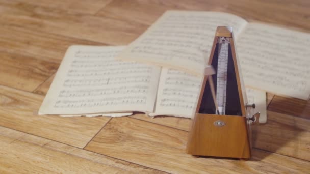 Vintage μετρονόμος με ένα ασημένιο εκκρεμές χτυπάει ένα αργό ρυθμό, σε φόντο ένα ανοιχτό βιβλίο της μουσικά - Πλάνα, βίντεο