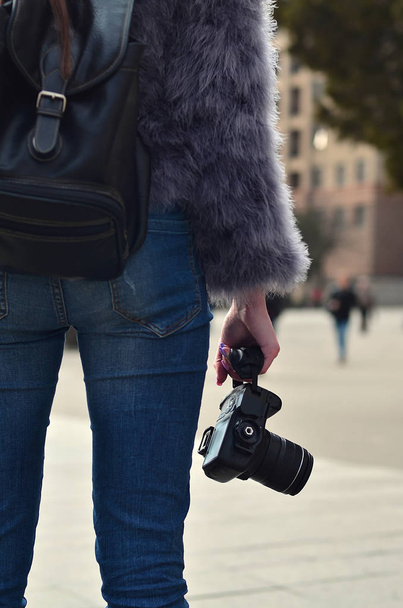 Rear view of a female photographer with a modern SLR camera in her hand against a blurred crowded street - Photo, Image