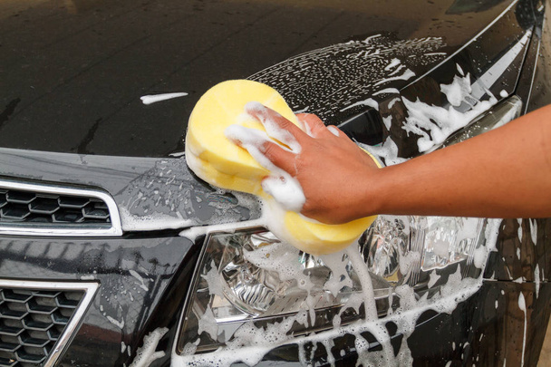 mano del Hombre lavando el coche usando la esponja amarilla con espuma
 - Foto, Imagen
