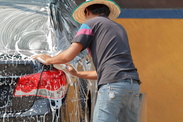 Man Aziatisch wassen de auto met behulp van de gele spons met schuim - Foto, afbeelding