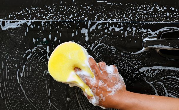 Uomo che lava l'auto usando la spugna gialla con schiuma
 . - Foto, immagini