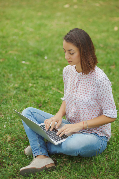 Jonge vrouw met laptop zittend op groen gras - Foto, afbeelding