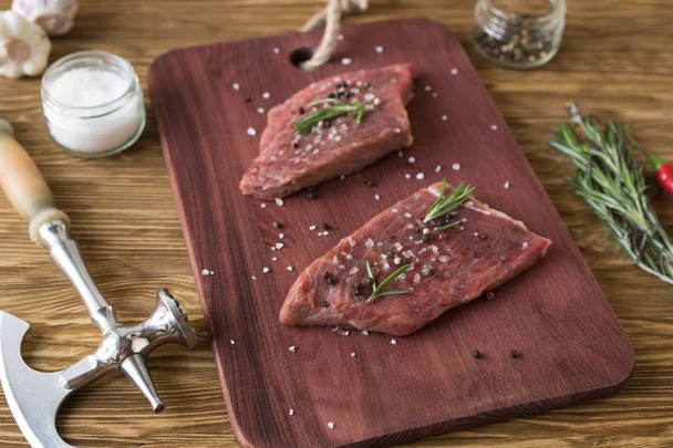 frische rohe Steaks mit Rosmarin und Knoblauch auf Holztisch - Foto, Bild