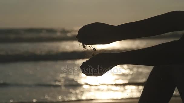 Рука молодої жінки, що грає з піском. Жіноча рука проливає морський пісок крізь пальці на заході сонця на океанському тлі. Повільний рух крупним планом
 - Кадри, відео