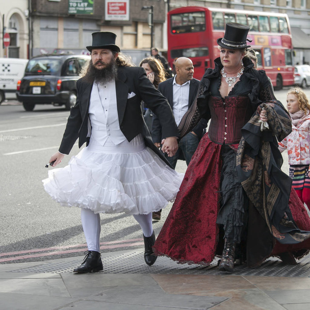 A man in a white wedding dress and a top hat with a woman in a gothic red velvet dress walking down the street in London Bridge - Foto, Imagem