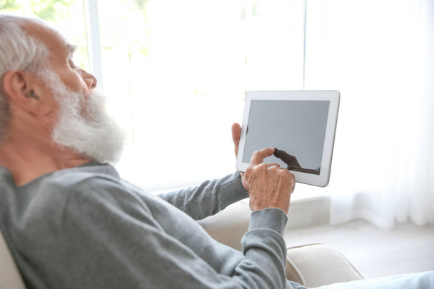 Senior man sitting on sofa with tablet - Фото, зображення