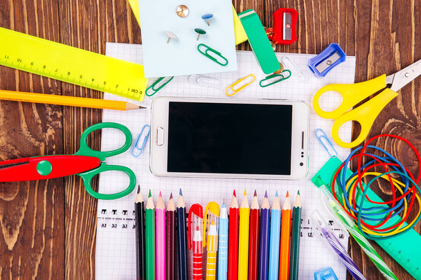 Nyitott üres notebook, fehér smartphone-val keret iskola készletek egy fából készült asztal háttere. Vissza a concept iskolai. - Fotó, kép