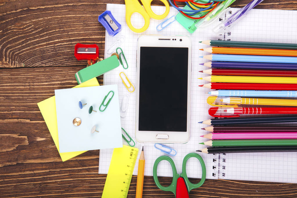 Open blank notebook, white smartphone with frame of school supplies on a wooden table background. Back to school concept. - Photo, Image