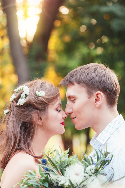 Happy young newlywed couple touching noses in park. Holding a bouquet. Romantic  - Foto, Imagen