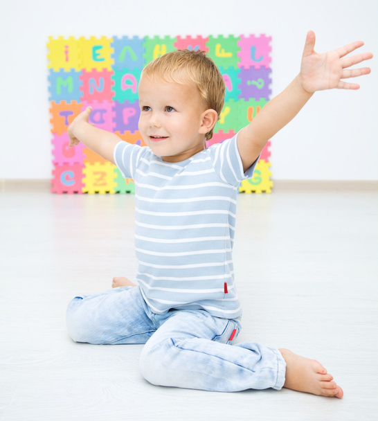 Little boy raised his hands while sitting on floor - Foto, Imagen