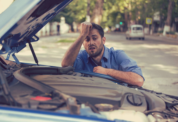 Мужчина, испытывающий проблемы с разбитой машиной, в отчаянии смотрит на неисправный двигатель
 - Фото, изображение