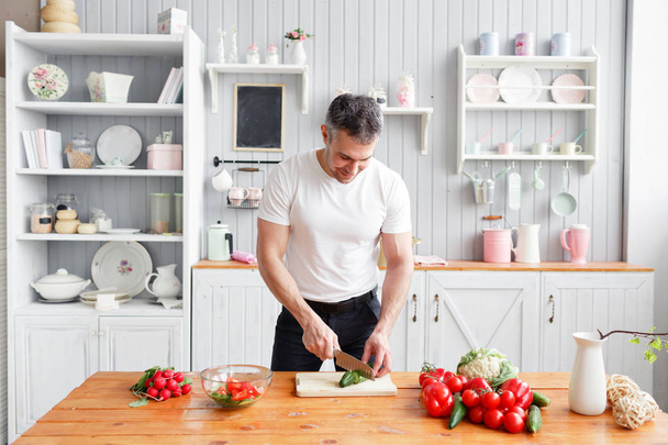 Middle-aged athlete, cuts vegetables salad of cucumber and tomato. Vegetarian food - Foto, Imagen