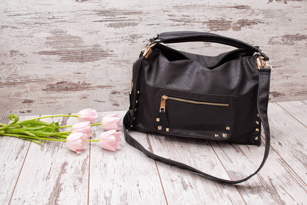 Черная сумка на деревянном фоне, розовые тюльпаны. Модная концепция
. - Фото, изображение