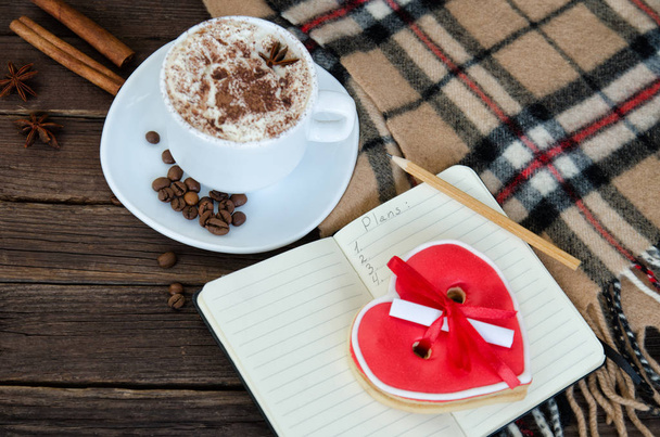 Gezellige rust. Mok latte, Kladblok met potlood, peperkoek-hart, geruite plaid en koffiebonen. Bovenaanzicht - Foto, afbeelding