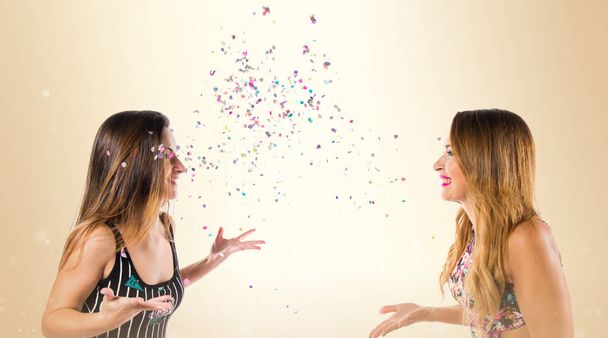 Chicas jóvenes felices con confeti en una fiesta sobre fondo ocre
 - Foto, imagen