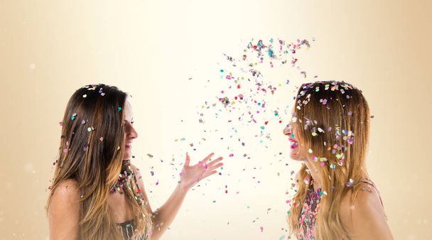 Счастливые девушки с конфетти на вечеринке на охровском фоне
 - Фото, изображение