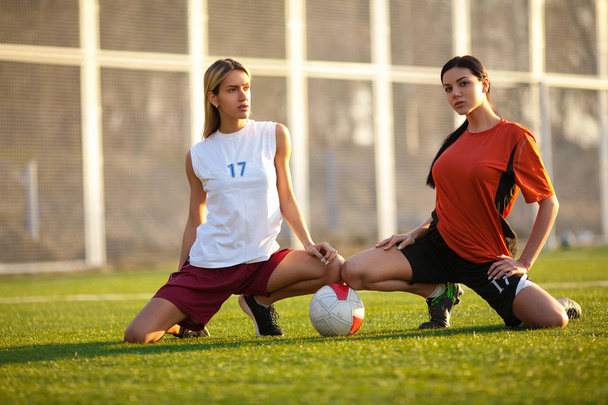 Twee meisjes in een uniform voetbal, zittend op een voetbal veld wit - Foto, afbeelding