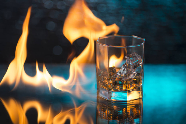 vaso de whisky con hielo sobre fondo azul y llamas de fuego
 - Foto, Imagen