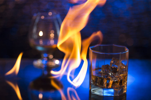 Glass o whisky with ice and wineglass of cognac and fire flames on bokeh background - Foto, immagini