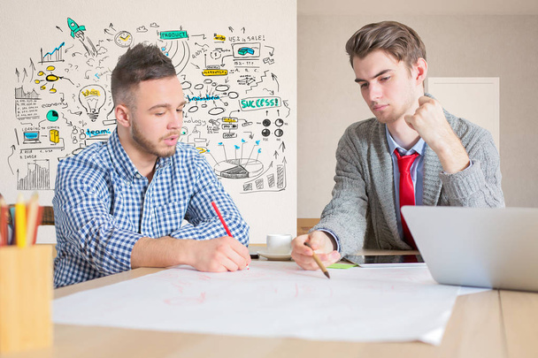 Portrait of two handsome young businessmen doing paperwork in modern office with creative business sketch. Teamwork concept - Photo, Image