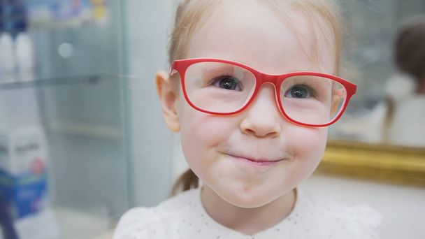 Little blonde girl in ophthalmology clinic plays with pink glasses - Photo, Image