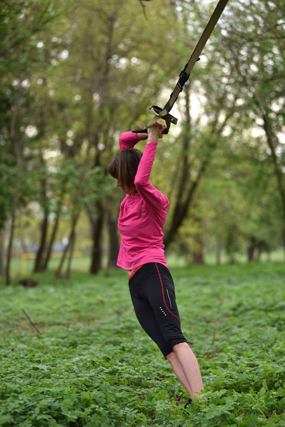 Young attractive woman does body stretching with trx fitness str - 写真・画像