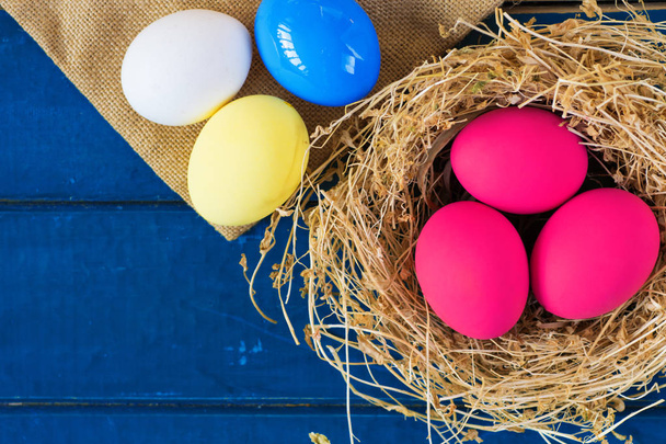 Colored eggs in nest on wooden background, selective focus image. Happy Easter Card - space for text - Foto, Imagem