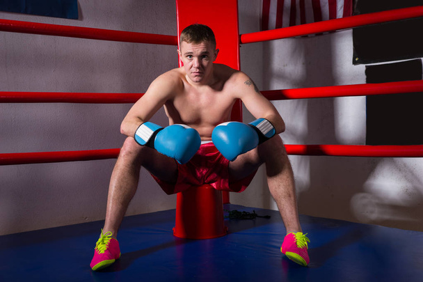 Young sporty male boxer with bare chest in boxing gloves sitting - Fotoğraf, Görsel
