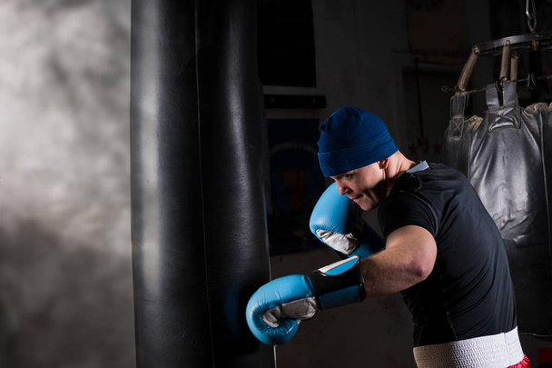 Young man in a hat and boxing gloves training with boxing punchi - Foto, Imagem