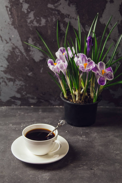 Auf dem Tisch liegt eine Tasse Kaffee und eine Vase mit Blumen Krokusse auf dem Hintergrund der Loft-Wand - Foto, Bild