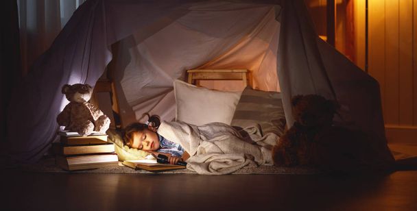 child girl sleeping in tent with  book and flashlight - Photo, Image