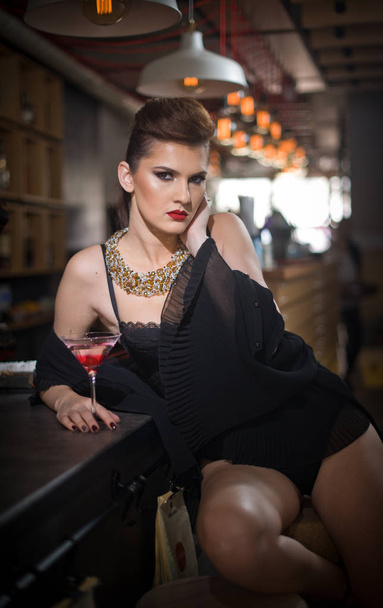Sensual girl with long legs and high heels sitting on the chair in bar  drinking .Handsome girl wearing beautiful body and high heels in indoor scene.Fashion model with long sexy legs drink cocktail. - Photo, image