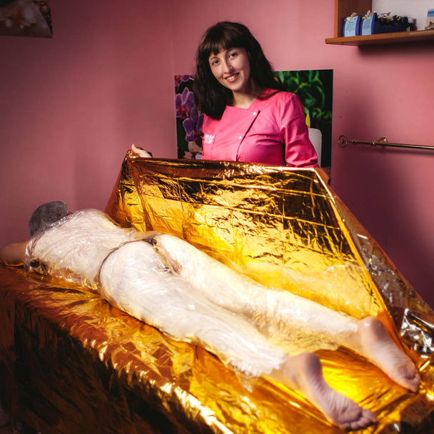 The girl lies on a massage table in foil - Foto, afbeelding