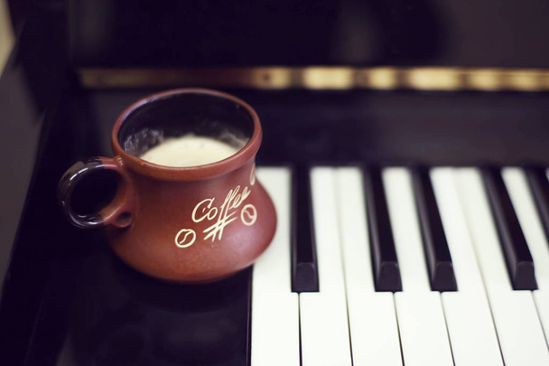 Cup of coffee on an old piano keyboard while composing. Evening time and some sun rays. Coffee mug on the piano keyboard - Photo, Image