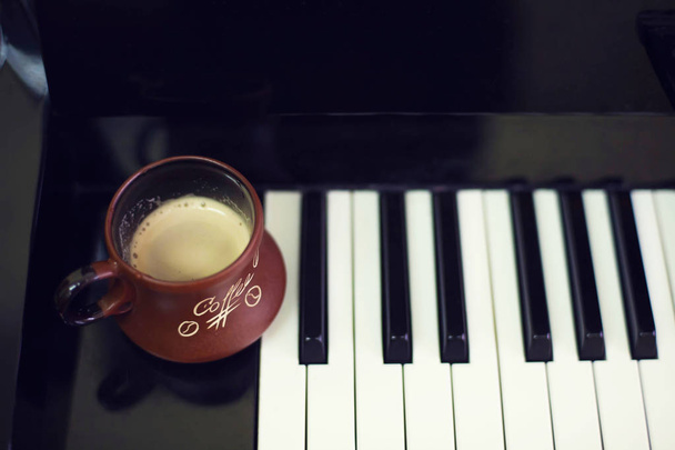Bir fincan kahve oluştururken bir eski piyano klavye üzerinde. Akşam saat ve bazı güneş ışınları. Piyano klavye üzerinde kahve kupa - Fotoğraf, Görsel