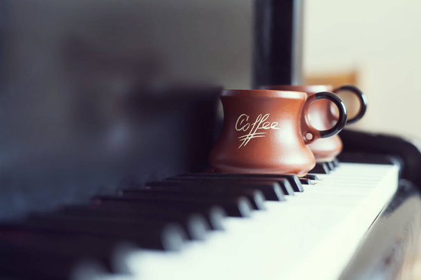 Φλιτζάνι του καφέ σε ένα παλιό πιάνο πληκτρολόγιο κατά τη σύνταξη. Φορά το βράδυ και μερικές ακτίνες του ήλιου. Κούπα καφέ στο πιάνο πληκτρολόγιο - Φωτογραφία, εικόνα
