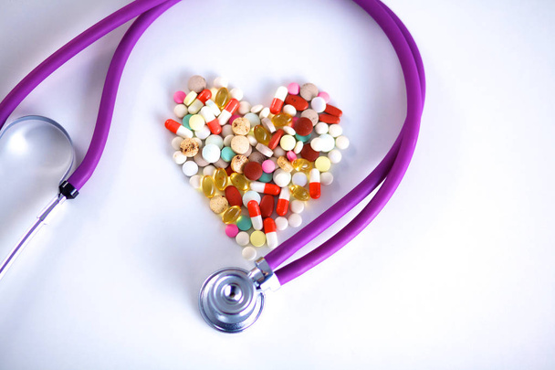 Крупный план таблеток, разбросанных по столу со стетоскопом и лежащим рядом сердцем
 - Фото, изображение