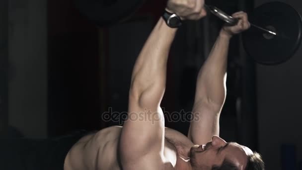Bodybuilder with naked torso lifting a barbell on a bench, tilt down - Footage, Video