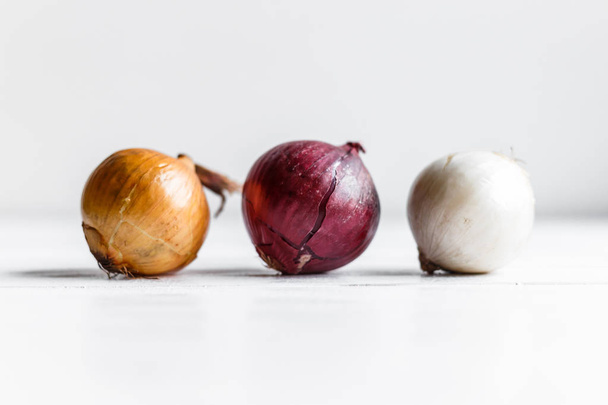 Τρεις βολβούς σε λευκό φόντο ξύλινη. Άσπρα κρεμμύδια, κρεμμύδια και κόκκινα κρεμμύδια - Φωτογραφία, εικόνα