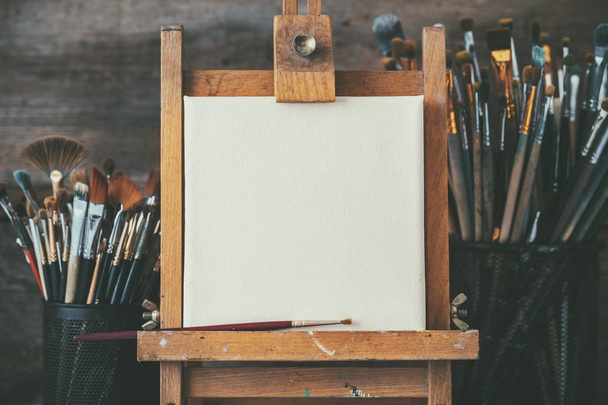Artistic equipment in a artist studio: artist canvas on wooden easel and paint brushes. - Foto, Imagem