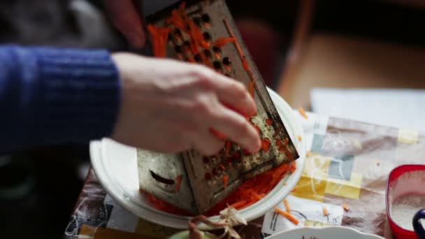 Kobieta pociera marchewki na tarce na deskę do krojenia - Materiał filmowy, wideo