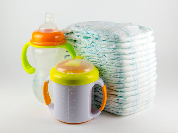 Fraldas e garrafas de bebê em um fundo branco
 - Foto, Imagem