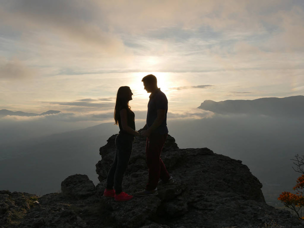 Силуети молодої пари стоять на горі і дивляться один на одного на красивому фоні заходу сонця. Любов хлопця і дівчинки
. - Фото, зображення