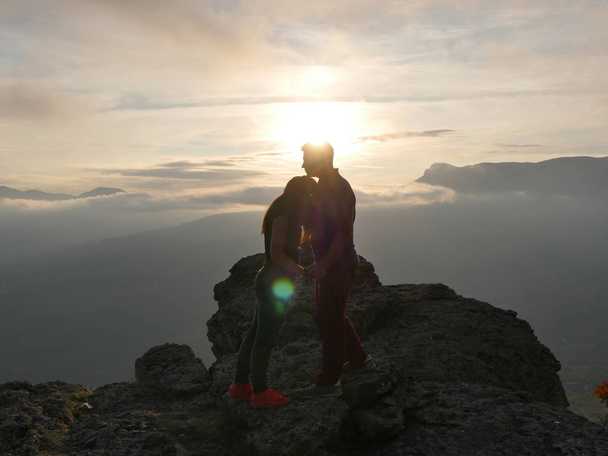 Σιλουέτες από νεαρό ζευγάρι που στέκεται πάνω σε ένα βουνό και να ψάχνουν κάθε άλλο όμορφο ηλιοβασίλεμα φόντο. Αγάπη ο τύπος και το κορίτσι. - Φωτογραφία, εικόνα
